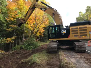 Clearing brush and trees on side of road with backhoe